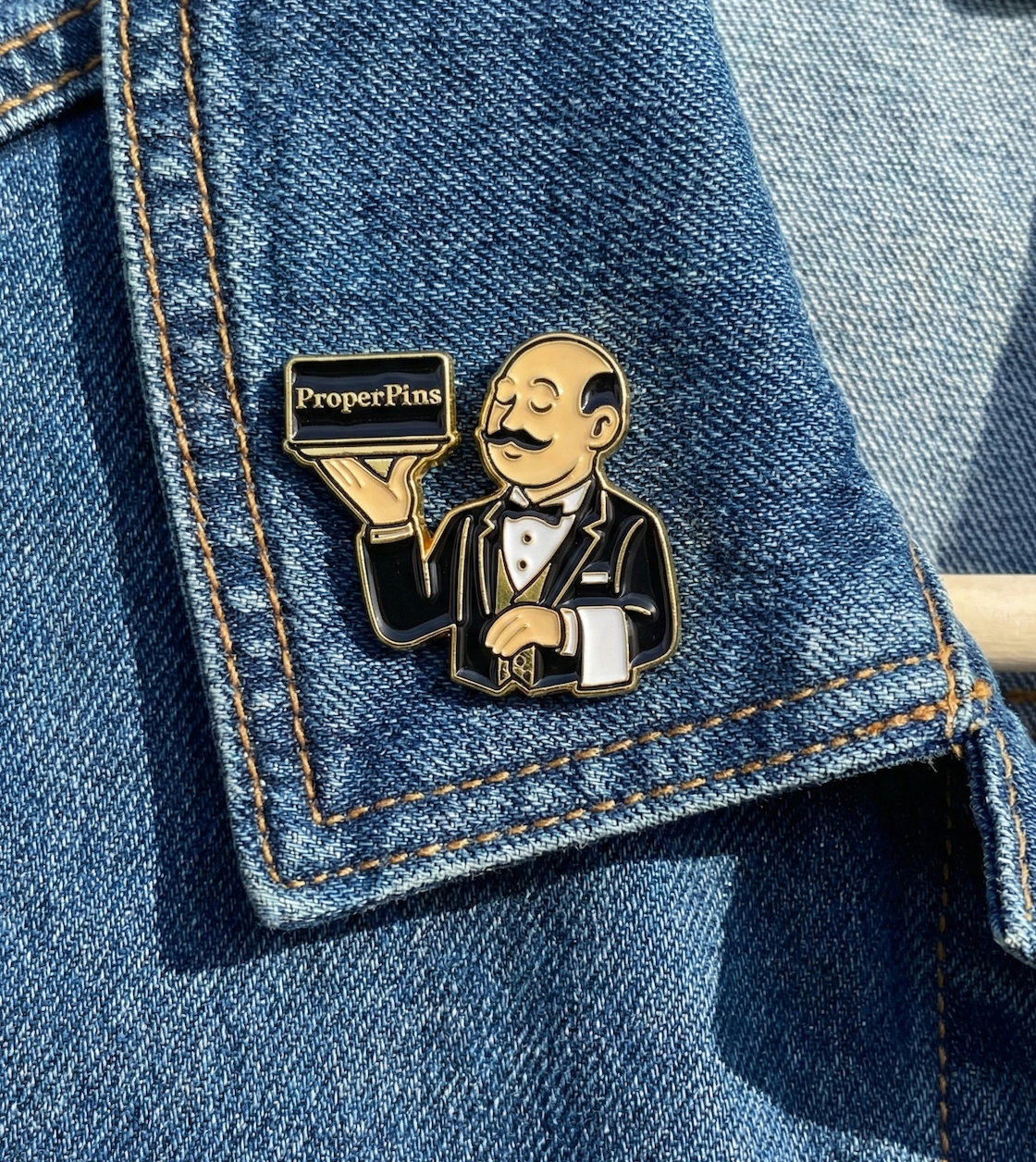 Custom soft enamel pin example - ProperPins butler mascot character holding a serving tray on denim jacket